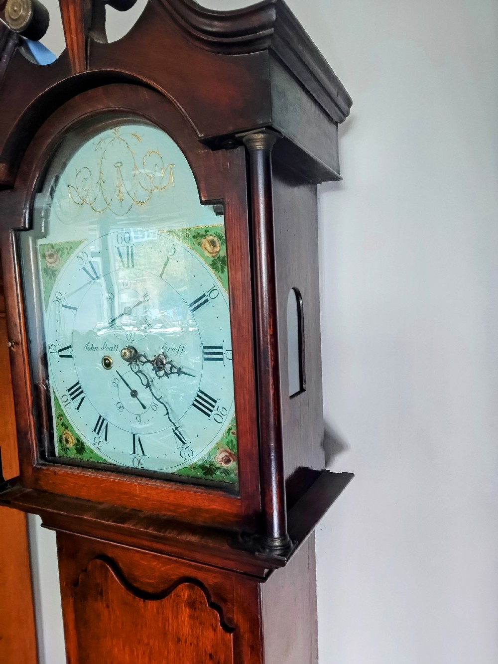 A Georgian oak and mahogany longcase clock featuring a swan-neck pediment, brass patera ornaments, fluted columns, and a painted arch dial. View V
