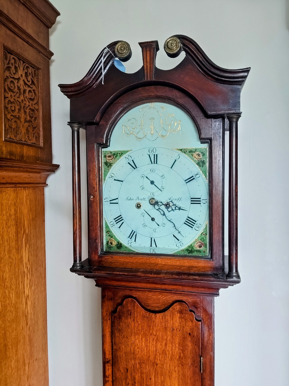 A Georgian oak and mahogany longcase clock featuring a swan-neck pediment, brass patera ornaments, fluted columns, and a painted arch dial. View VIII