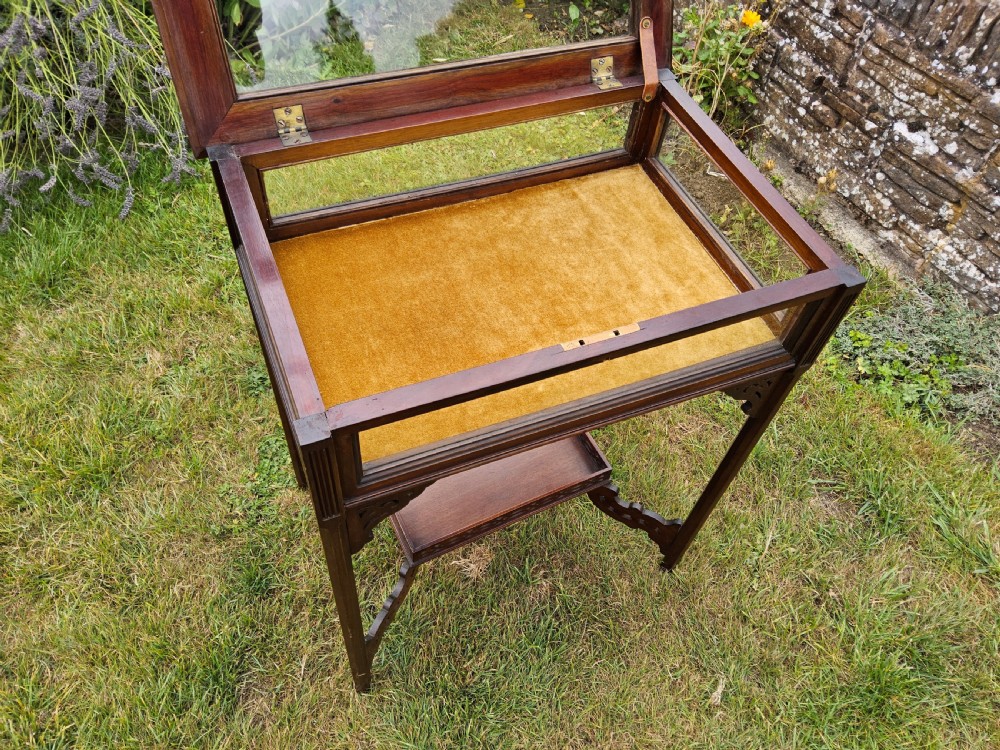 A rectangular dark mahogany bijouterie table featuring glazed sides and top, a gold fabric lining inside, pierced fretwork corner spandrels, and a lower tier shelf with a fretwork gallery. View II