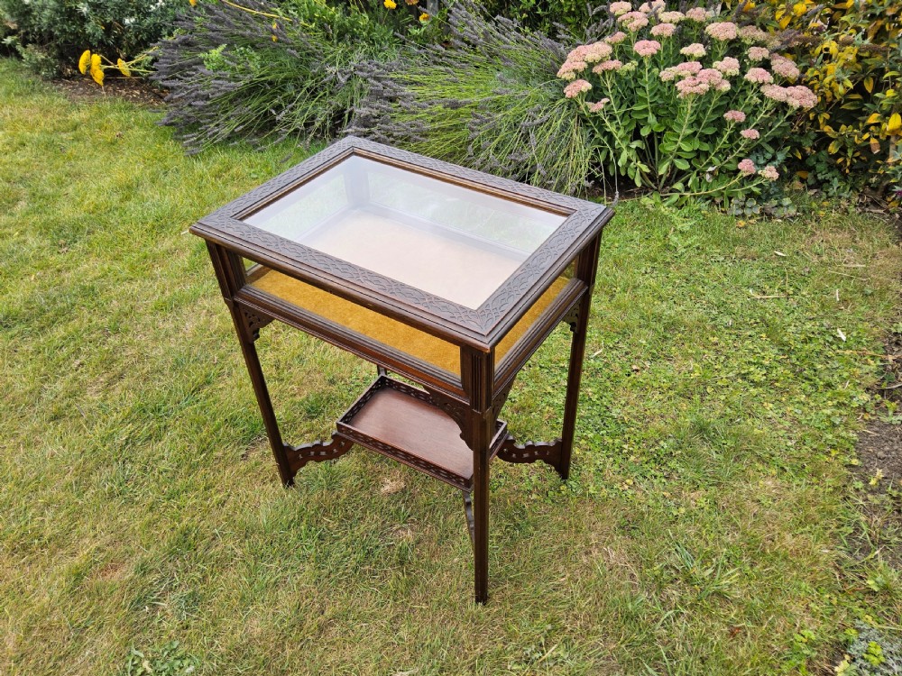 A rectangular dark mahogany bijouterie table featuring glazed sides and top, a gold fabric lining inside, pierced fretwork corner spandrels, and a lower tier shelf with a fretwork gallery. View IV