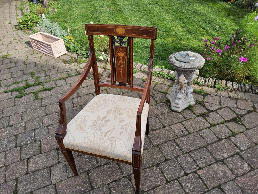 An Edwardian mahogany elbow chair featuring decorative marquetry inlay on the backrest splat and a light patterned upholstered seat.