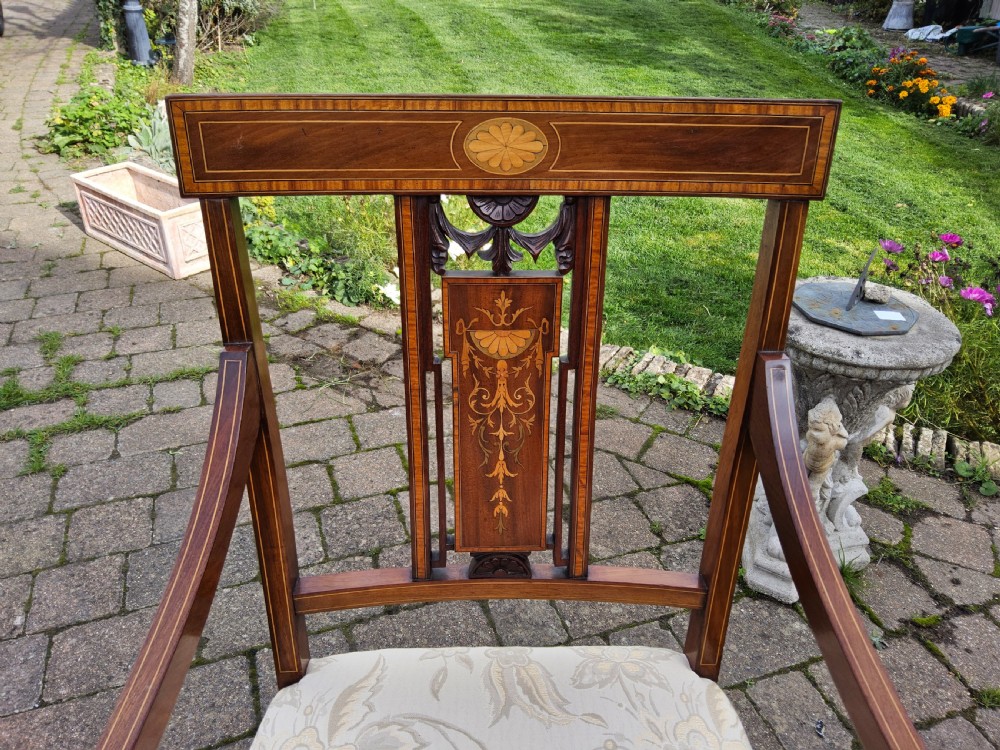 An Edwardian mahogany elbow chair featuring decorative marquetry inlay on the backrest splat and a light patterned upholstered seat. View II