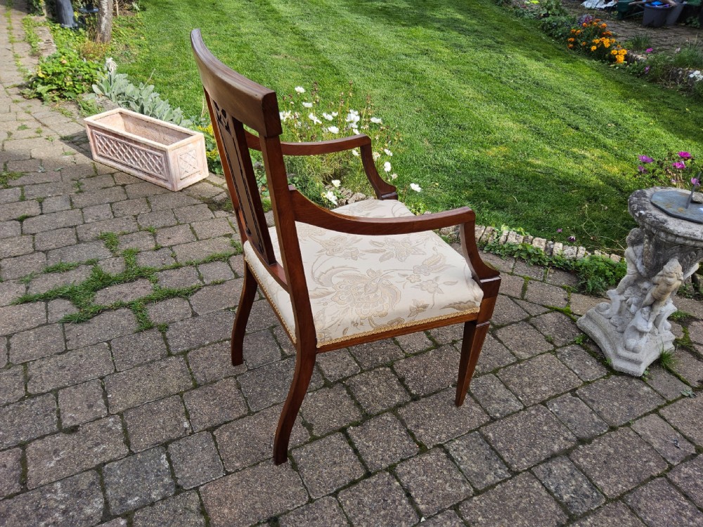 An Edwardian mahogany elbow chair featuring decorative marquetry inlay on the backrest splat and a light patterned upholstered seat. View V
