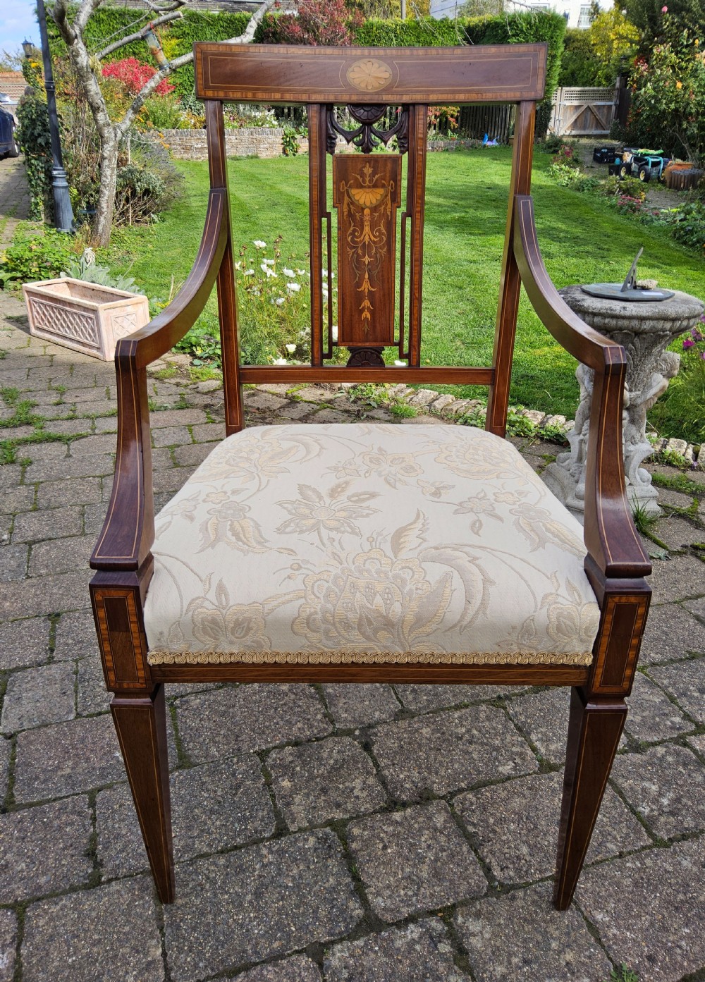 An Edwardian mahogany elbow chair featuring decorative marquetry inlay on the backrest splat and a light patterned upholstered seat. View IX