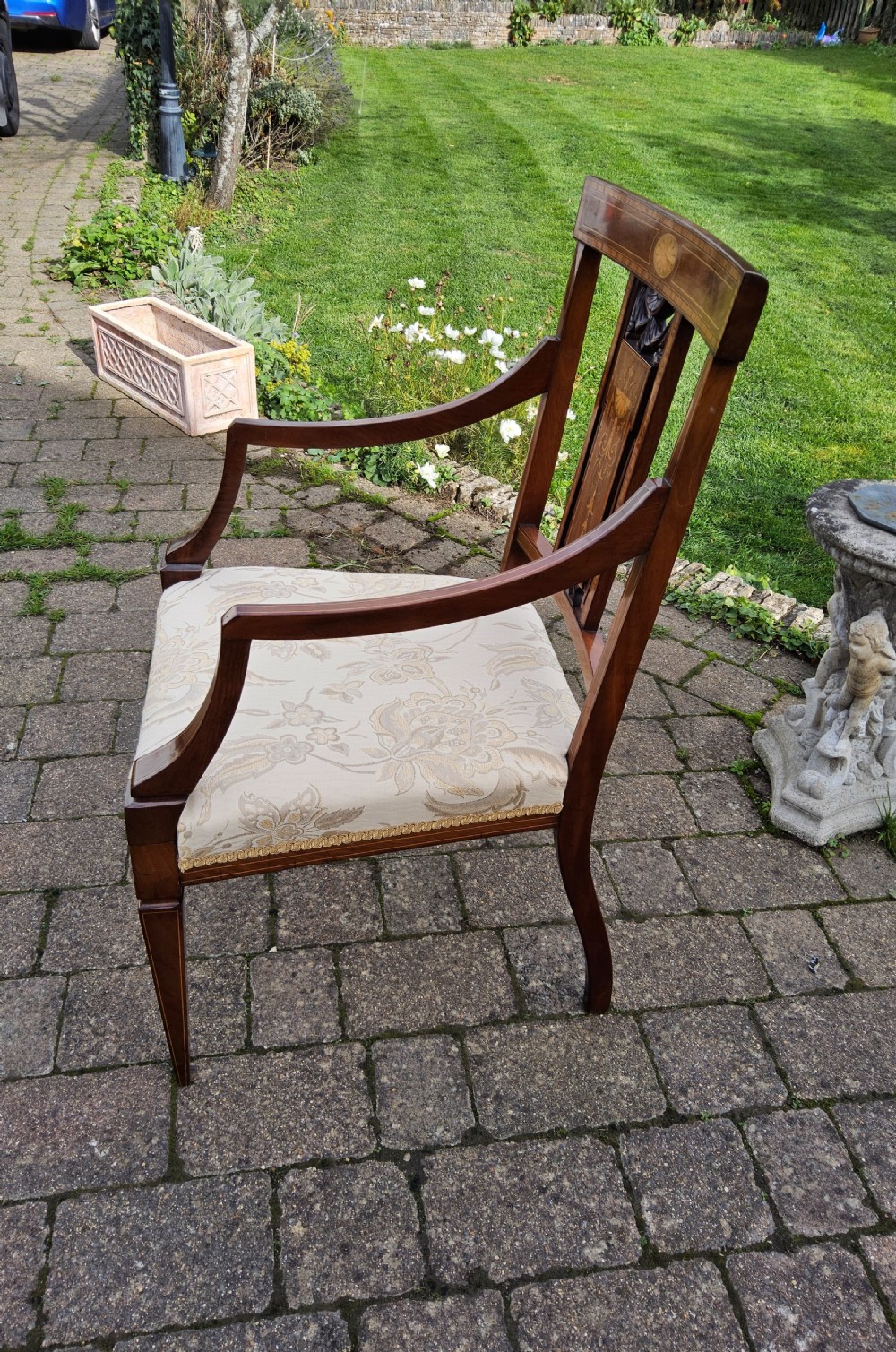An Edwardian mahogany elbow chair featuring decorative marquetry inlay on the backrest splat and a light patterned upholstered seat. View X