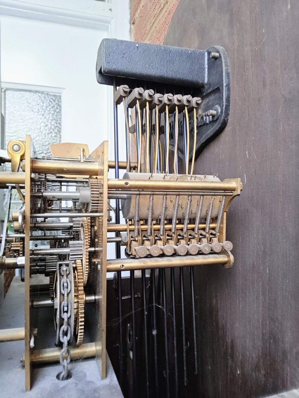 A traditional warm oak grandmother longcase clock featuring an arched top hood, silvered dial, glazed door revealing brass weights and pendulum, and a solid base. View VI