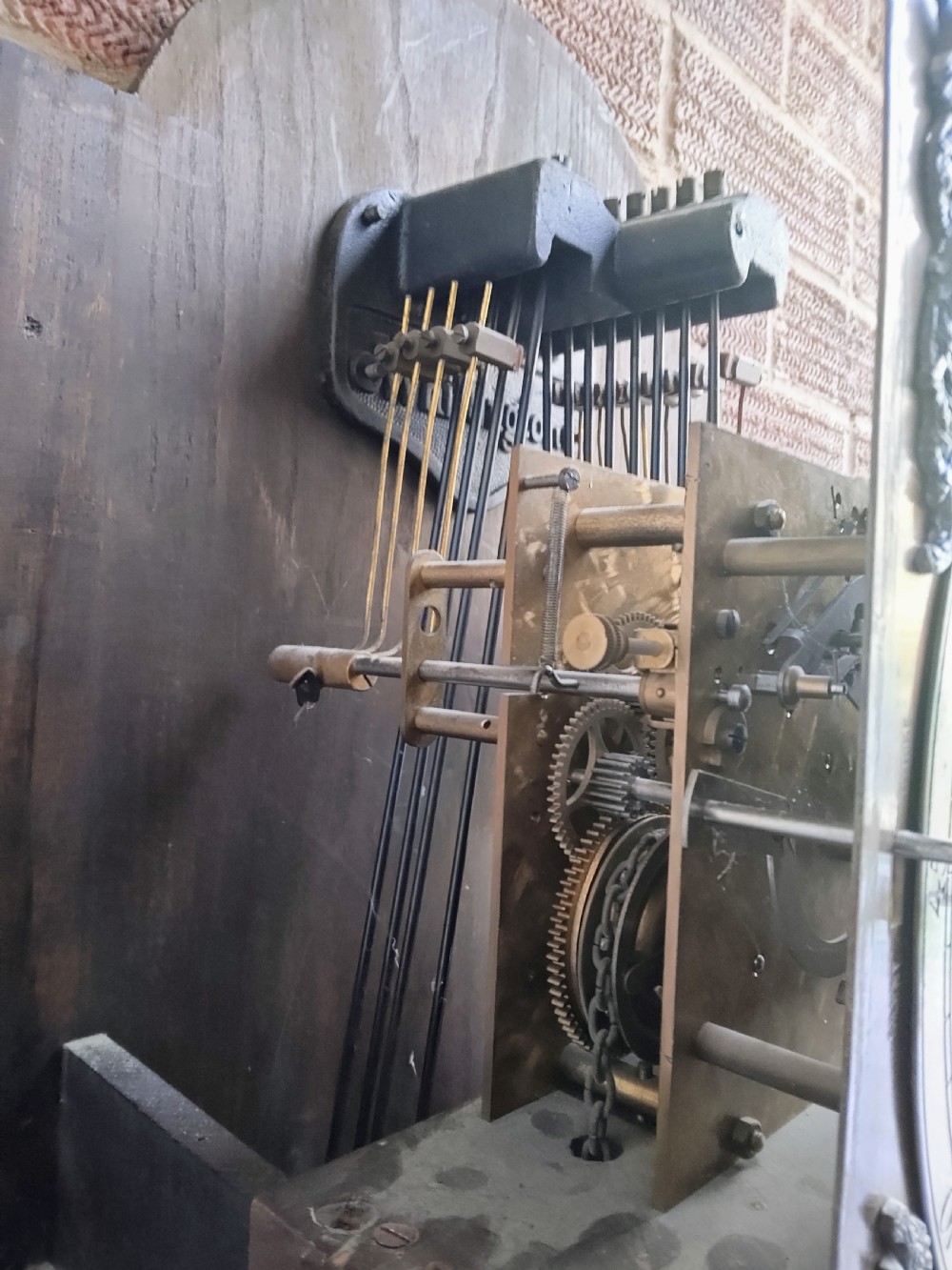 A traditional warm oak grandmother longcase clock featuring an arched top hood, silvered dial, glazed door revealing brass weights and pendulum, and a solid base. View VII