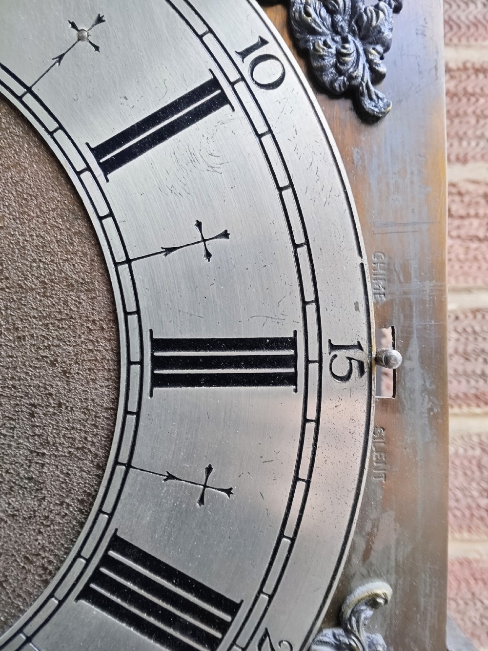A traditional warm oak grandmother longcase clock featuring an arched top hood, silvered dial, glazed door revealing brass weights and pendulum, and a solid base. View XIV