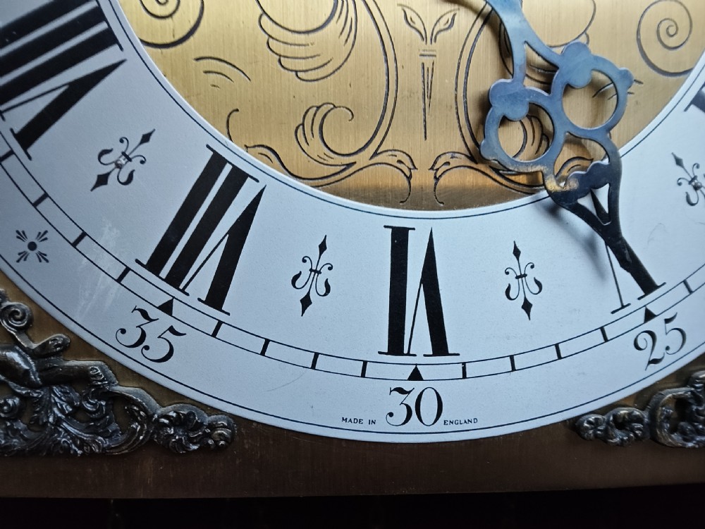 A slim mahogany grandmother longcase clock with a carved top frieze, brass Roman numeral dial, and an arched waist door. View VII
