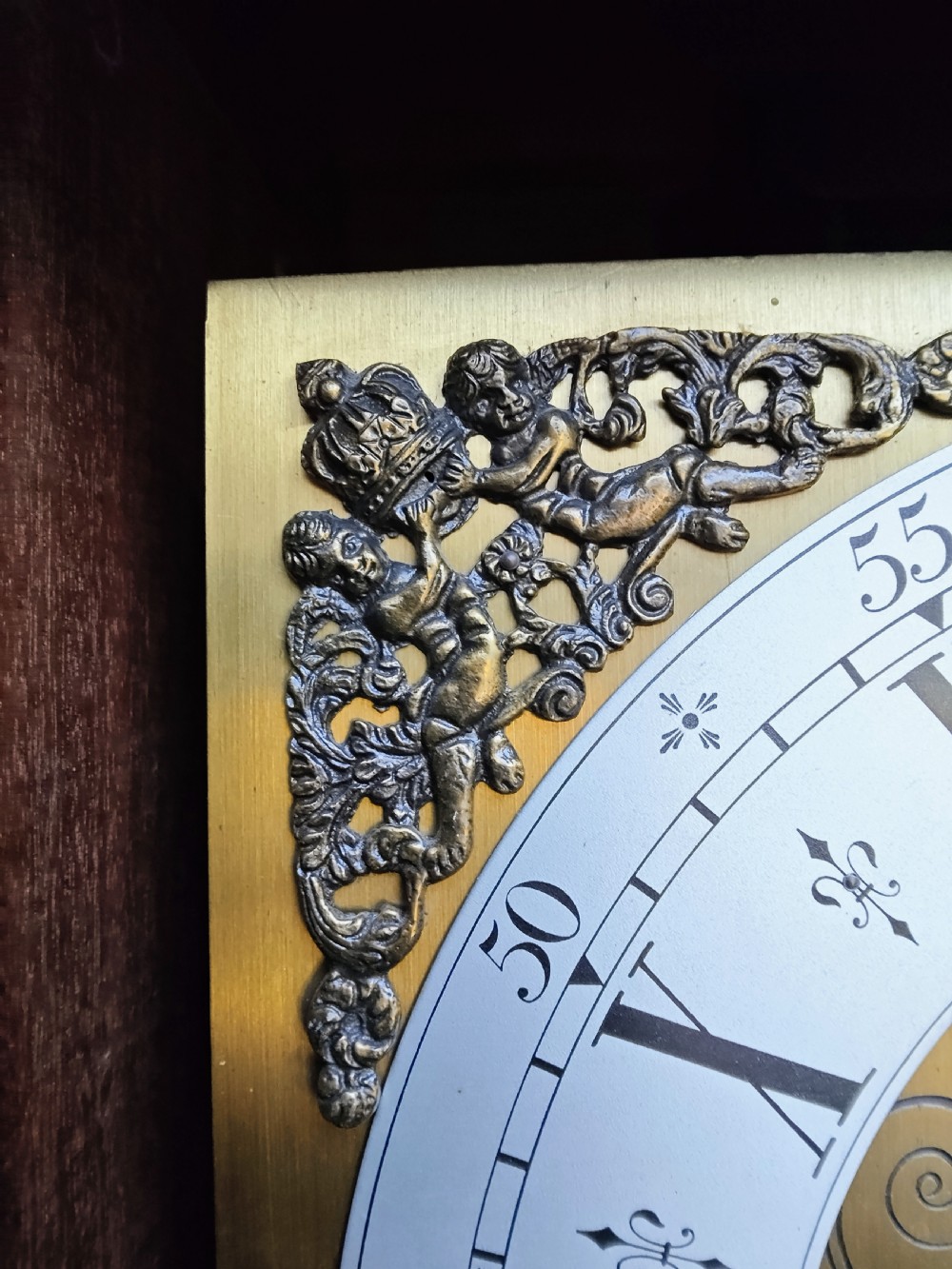 A slim mahogany grandmother longcase clock with a carved top frieze, brass Roman numeral dial, and an arched waist door. View IX