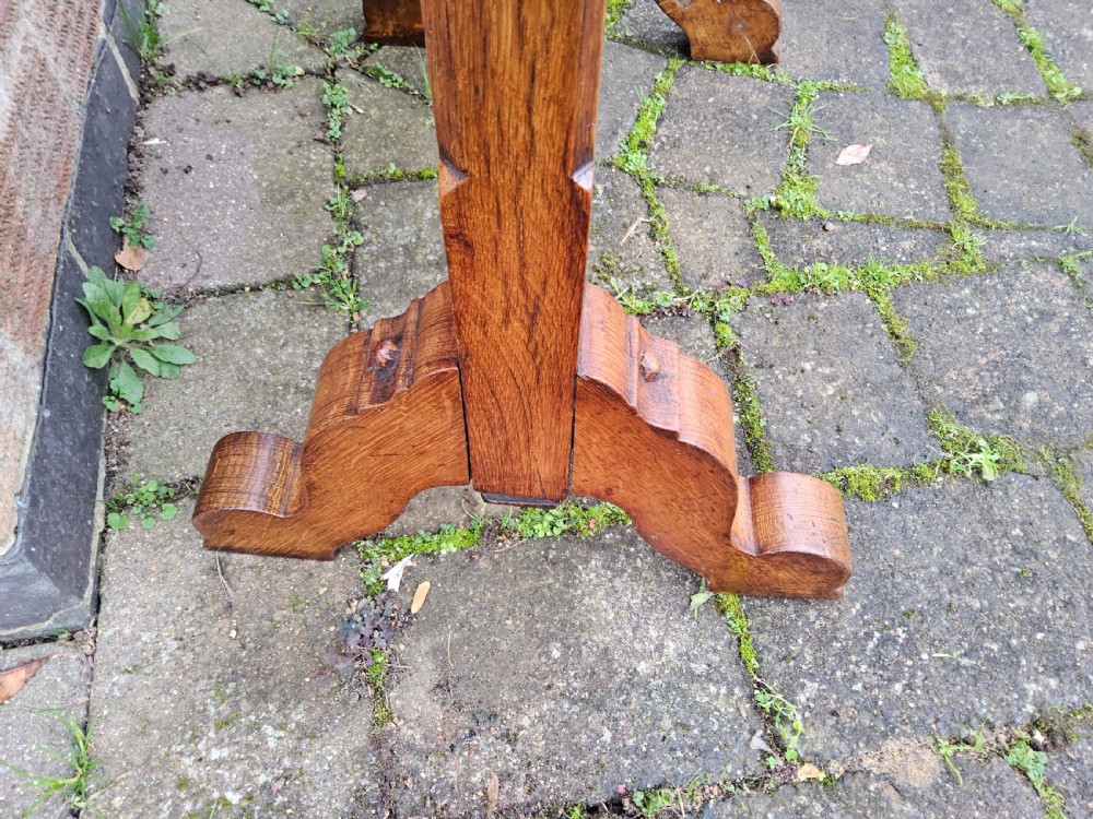 A freestanding Gothic Revival oak frame containing carved trefoil cut-outs, suspending a central circular hammered brass dinner gong with a wooden striker. View IX