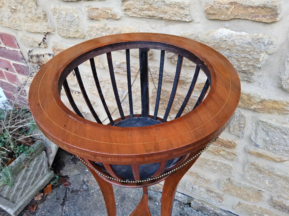 An Edwardian mahogany tripod jardiniere stand featuring slatted sides, satinwood stringing inlay around the top rim, three sweeping splayed legs, and a removable metal liner. View III