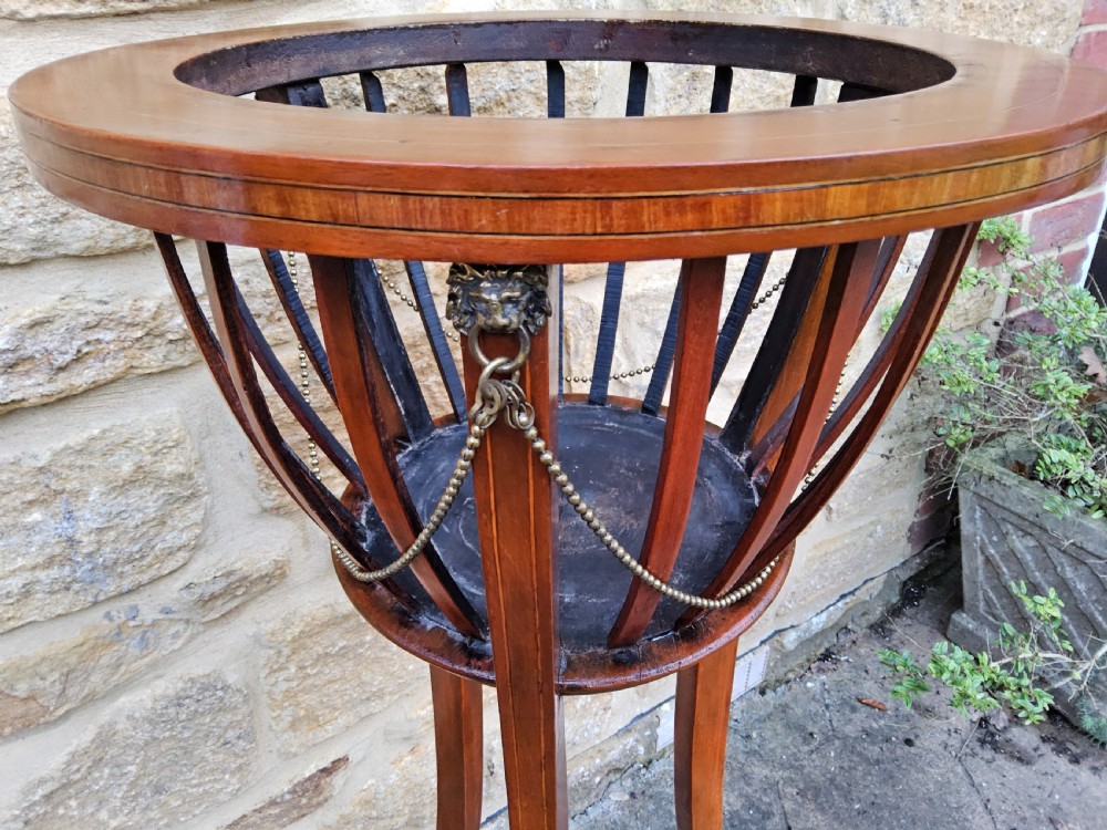 An Edwardian mahogany tripod jardiniere stand featuring slatted sides, satinwood stringing inlay around the top rim, three sweeping splayed legs, and a removable metal liner. View IV