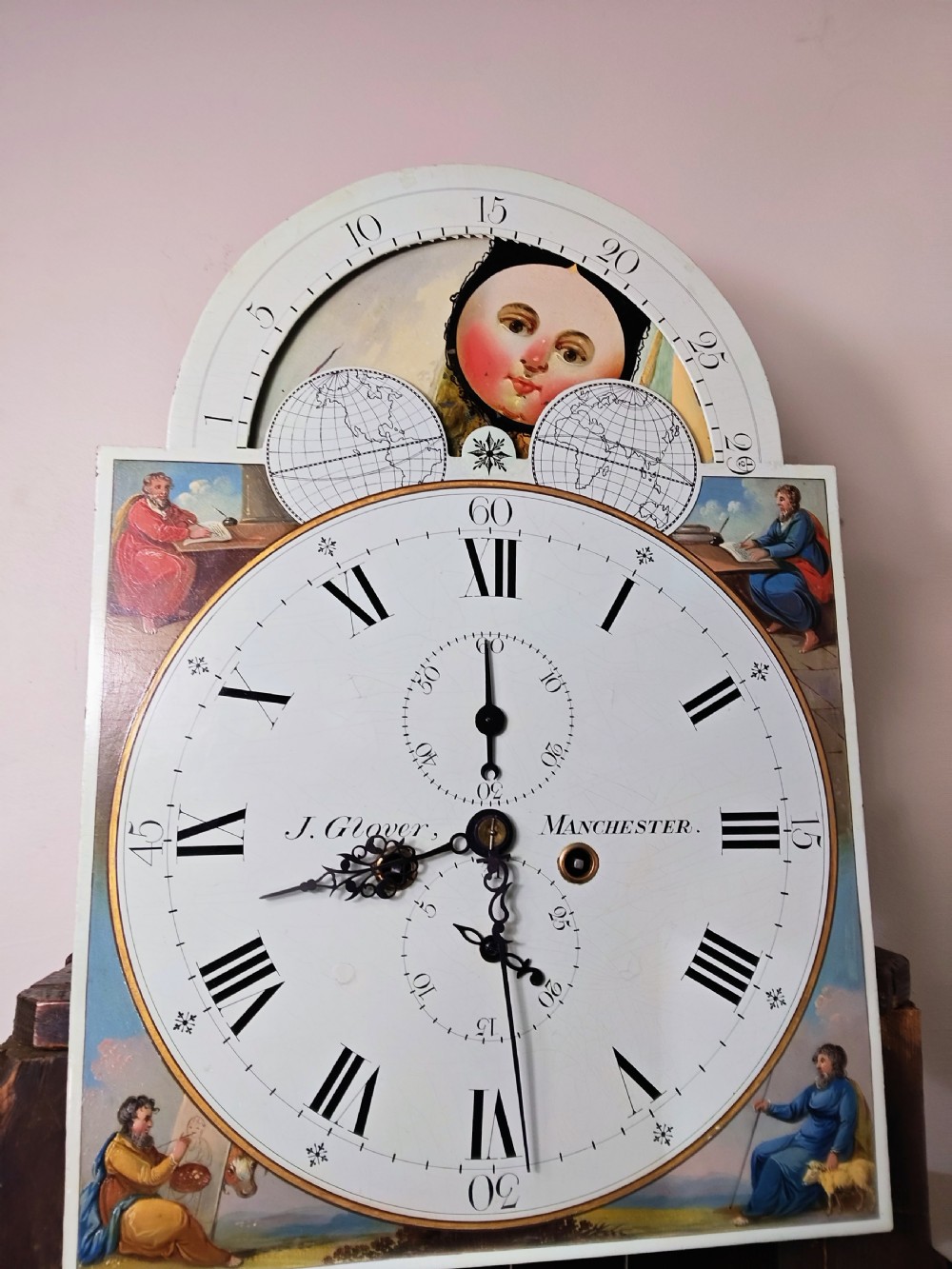 A Georgian flame mahogany longcase clock featuring a painted dial with moon phase indicator, swan-neck pediment, brass finials, and fluted columns. View XVII