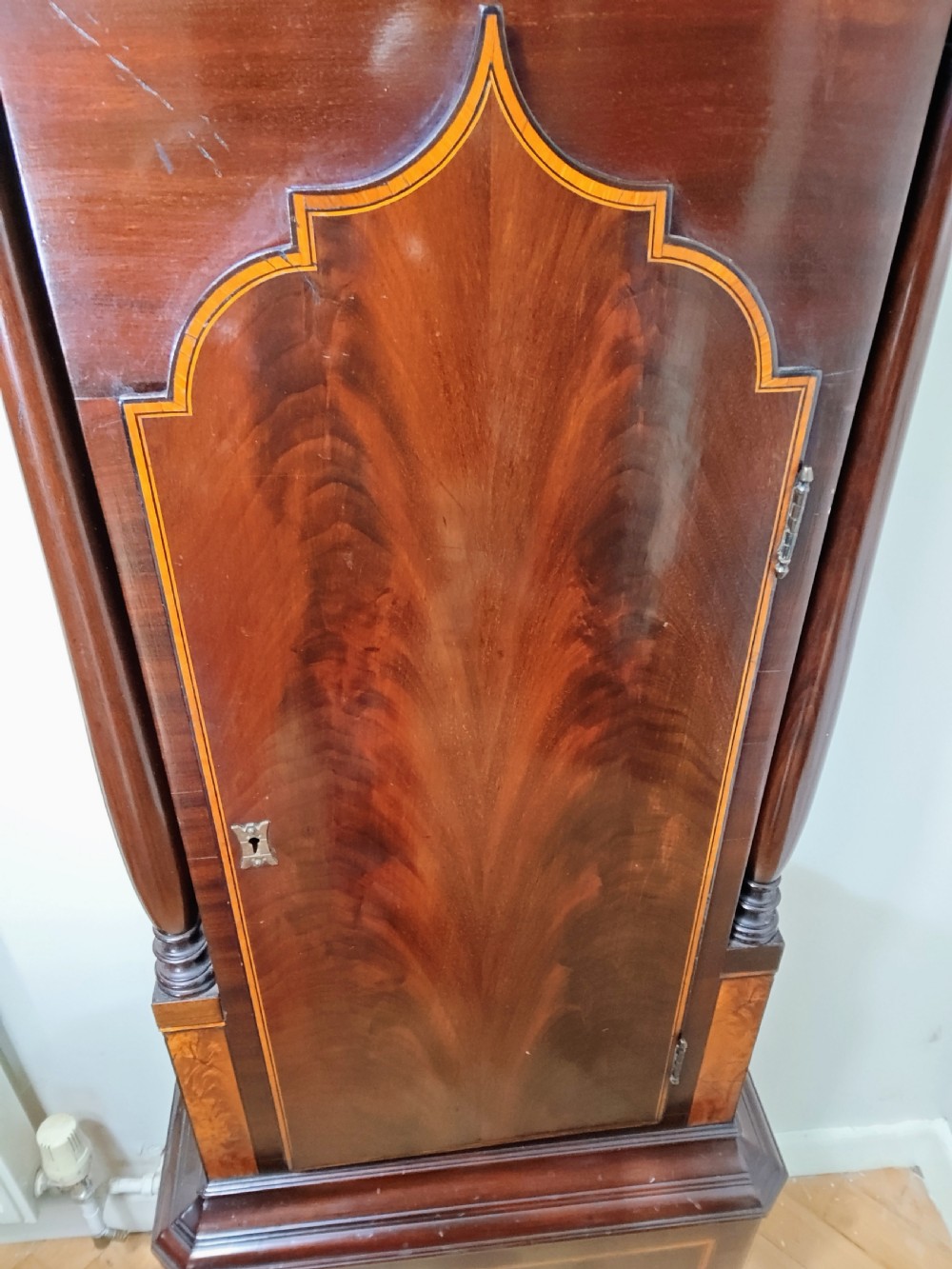 A Georgian flame mahogany longcase clock featuring a painted dial with moon phase indicator, swan-neck pediment, brass finials, and fluted columns. View XXII