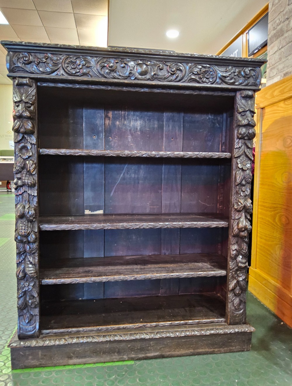 A dark oak Victorian open bookcase featuring hand-carved floral friezes, fruit garlands along the side columns, and adjustable shelving.
