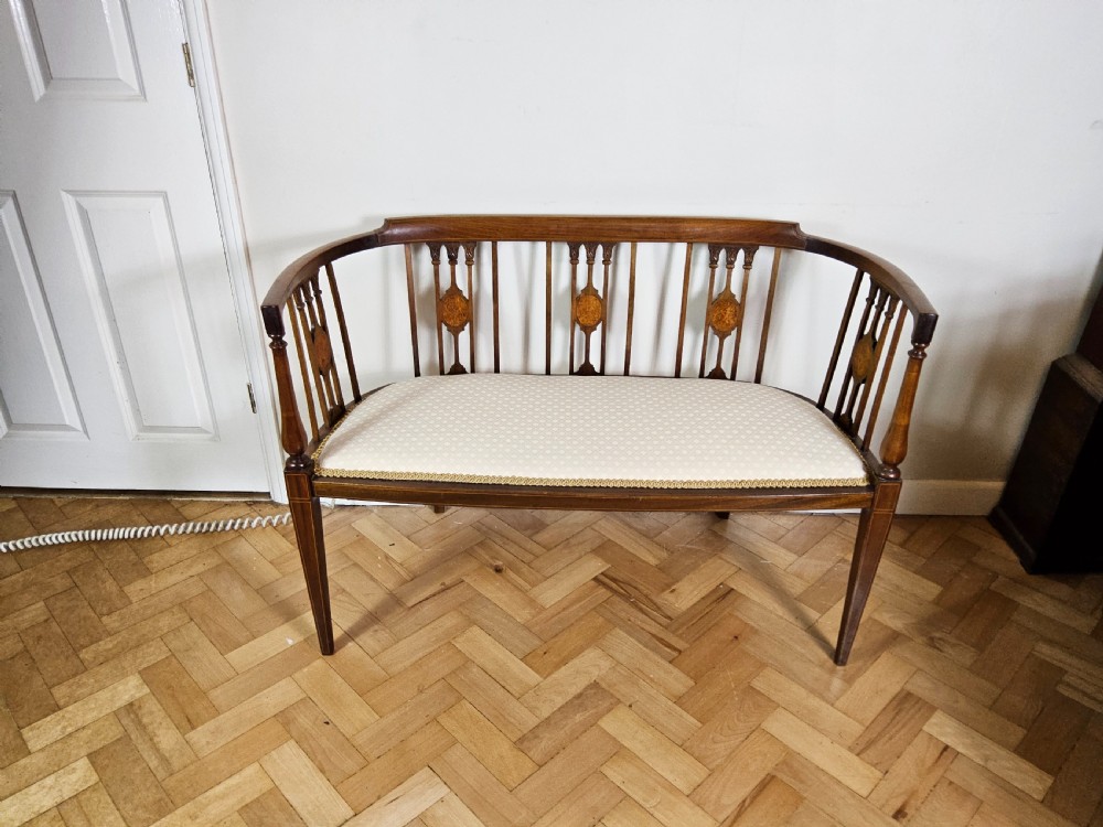 An Edwardian mahogany settee featuring a curved backrest with inlaid vertical splats, tapered legs, and a cream patterned upholstered seat.