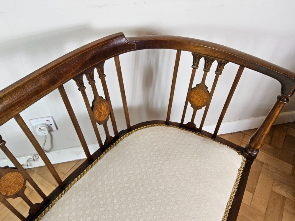 An Edwardian mahogany settee featuring a curved backrest with inlaid vertical splats, tapered legs, and a cream patterned upholstered seat. View IV