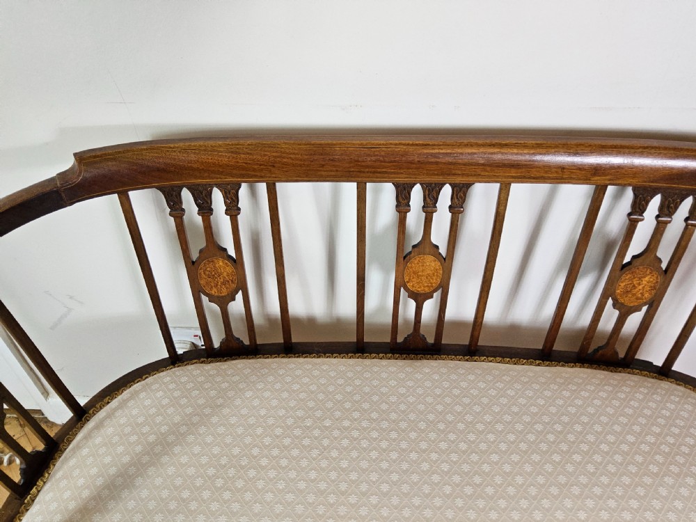An Edwardian mahogany settee featuring a curved backrest with inlaid vertical splats, tapered legs, and a cream patterned upholstered seat. View V