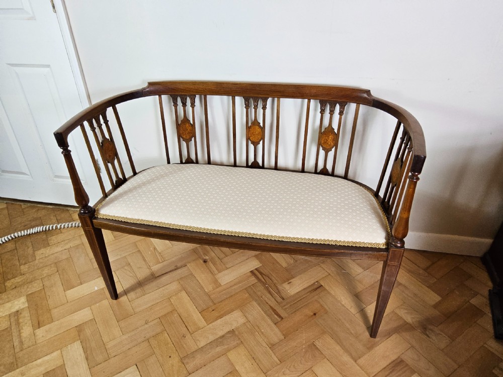 An Edwardian mahogany settee featuring a curved backrest with inlaid vertical splats, tapered legs, and a cream patterned upholstered seat. View VI