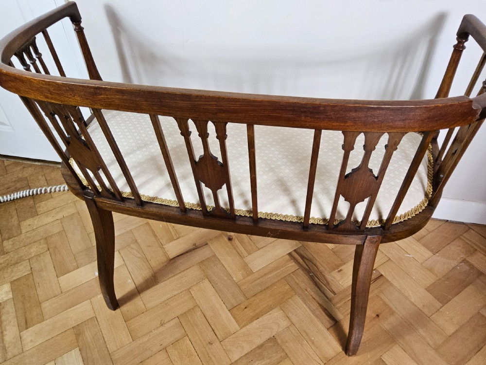 An Edwardian mahogany settee featuring a curved backrest with inlaid vertical splats, tapered legs, and a cream patterned upholstered seat. View VIII