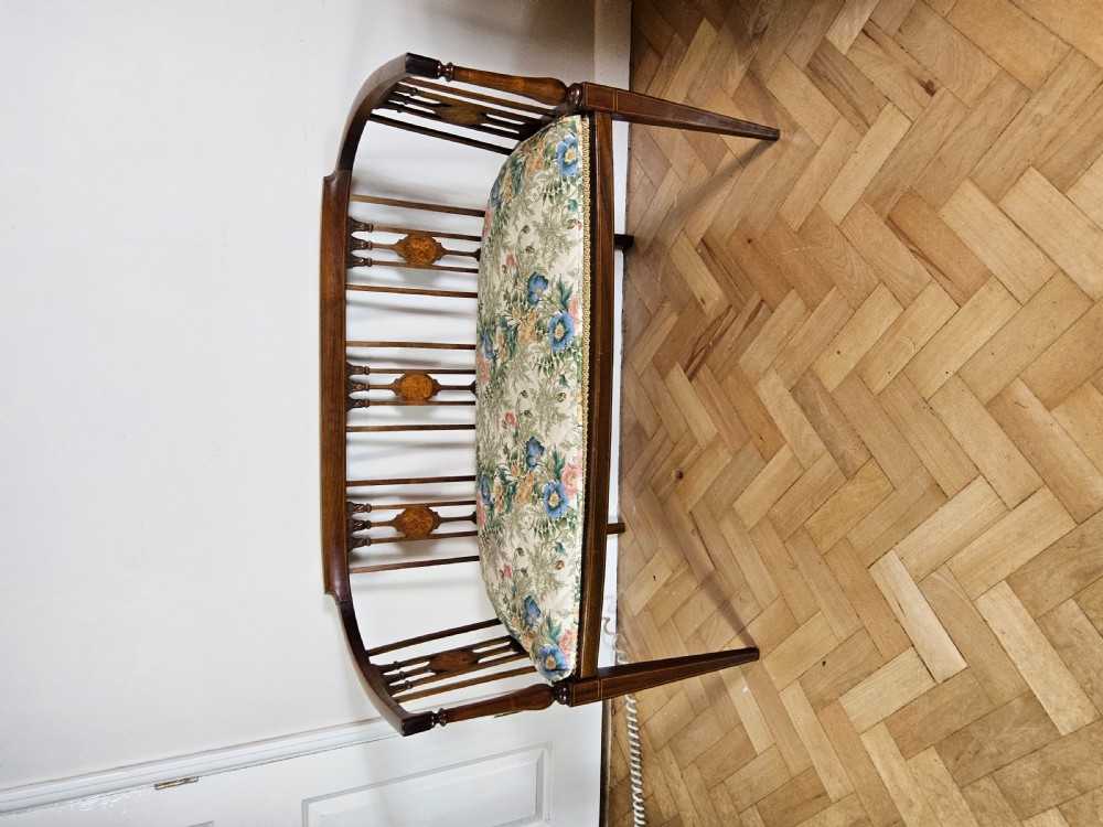 An Edwardian mahogany settee featuring a curved backrest with inlaid vertical splats, tapered legs, and a cream patterned upholstered seat. View IX