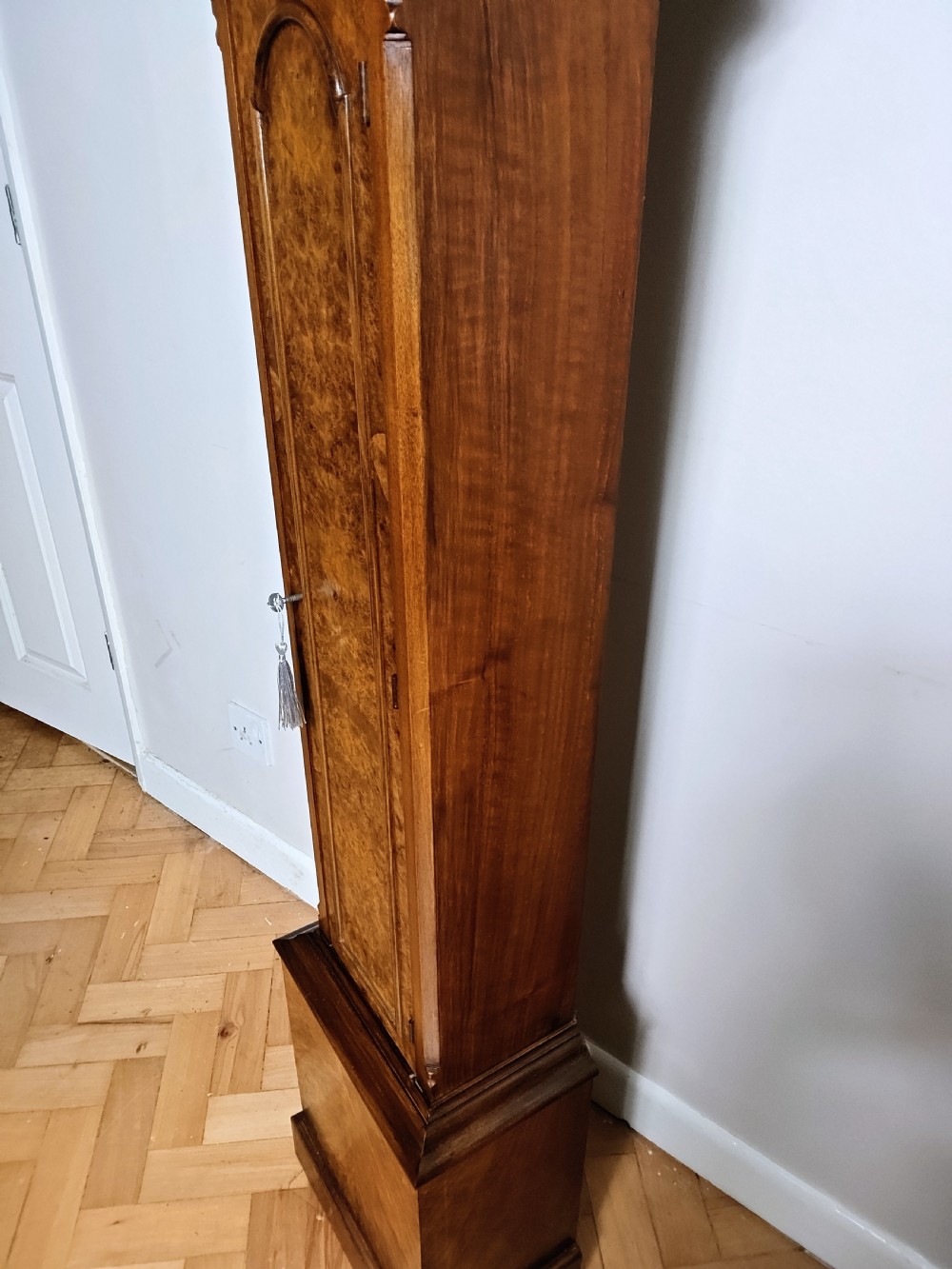 A tall burr walnut grandmother longcase clock featuring an arched hood, silvered dial with Roman numerals, and an arched trunk door. View V