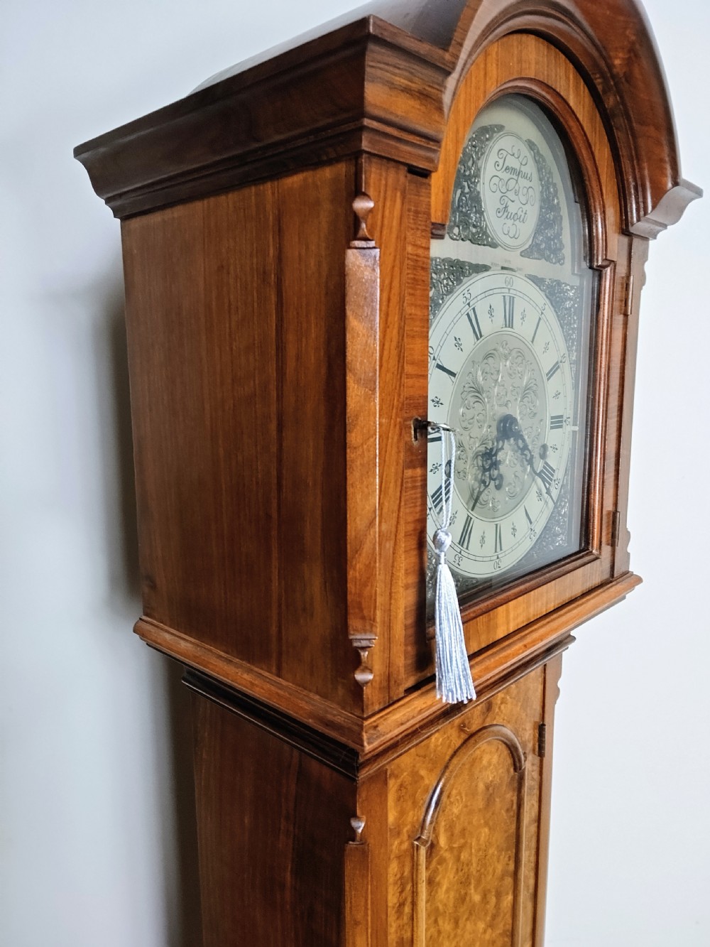 A tall burr walnut grandmother longcase clock featuring an arched hood, silvered dial with Roman numerals, and an arched trunk door. View VI