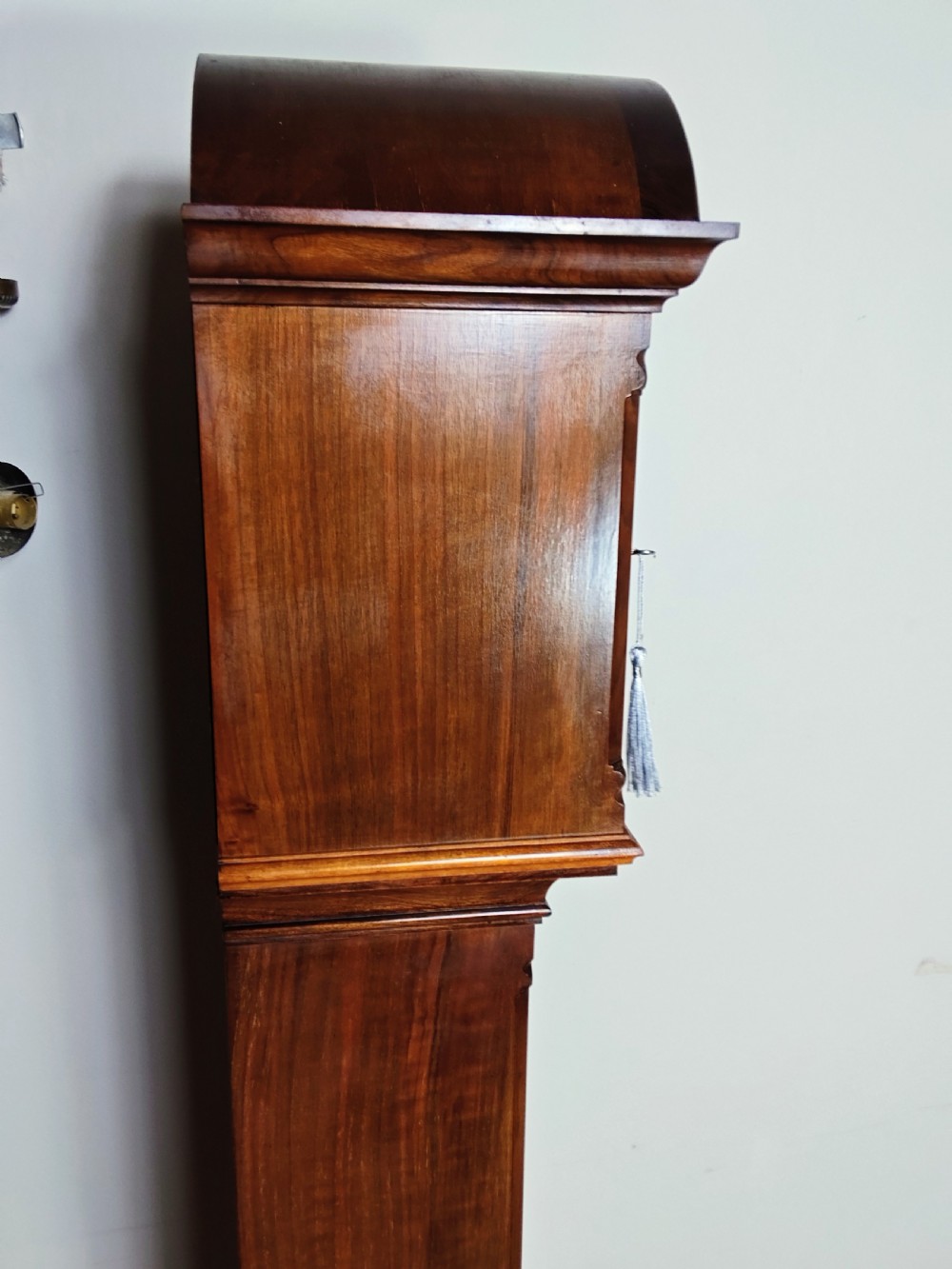 A tall burr walnut grandmother longcase clock featuring an arched hood, silvered dial with Roman numerals, and an arched trunk door. View IX