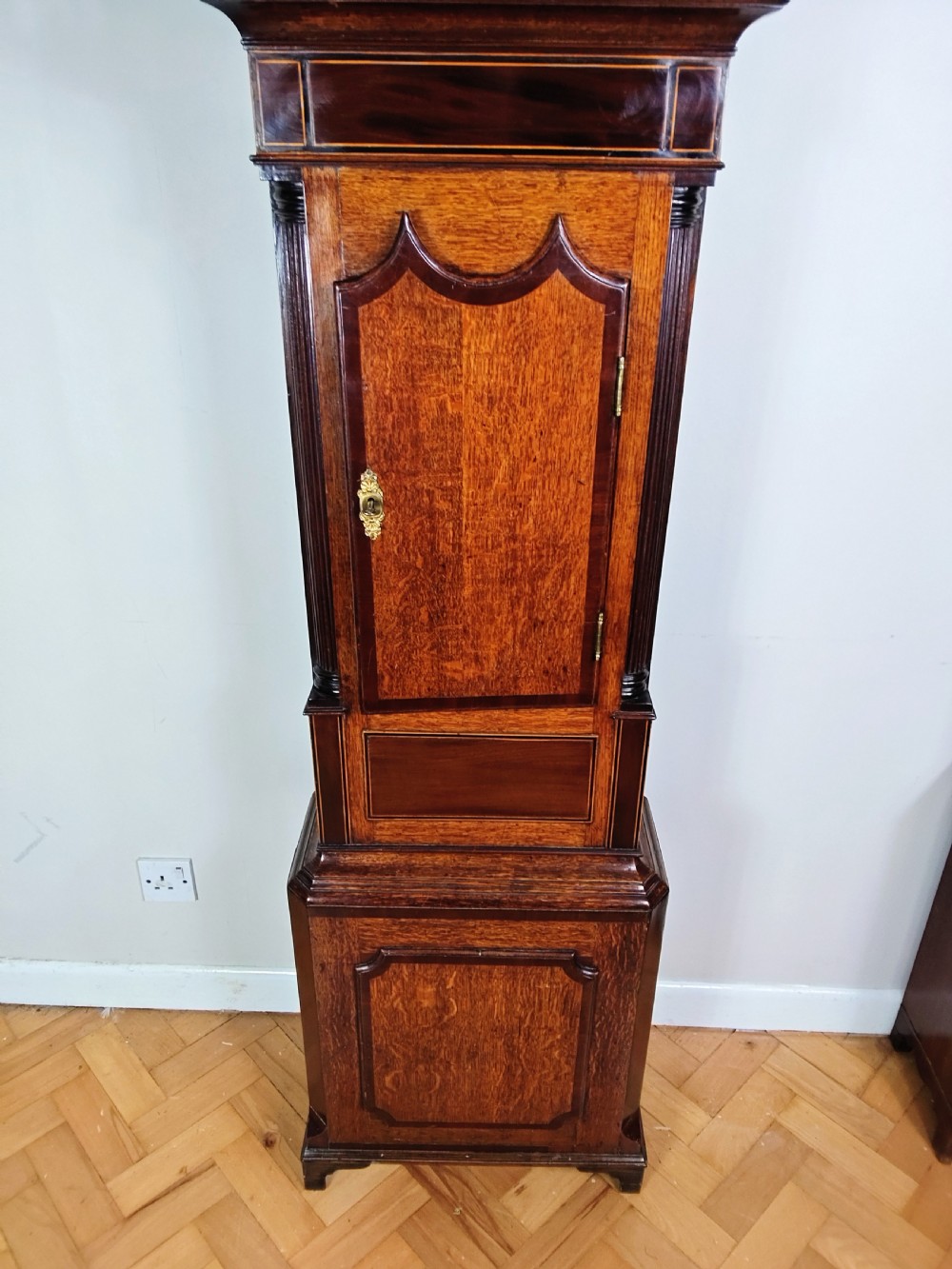 A Georgian oak and mahogany longcase clock featuring a swan-neck pediment, turned pillars, and a painted arch dial. View IV
