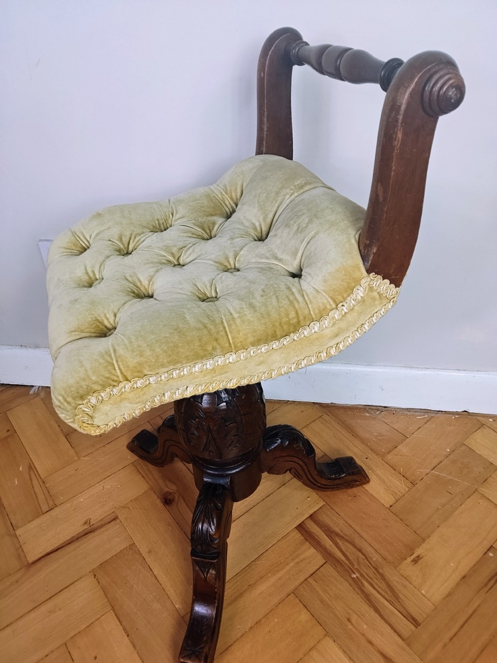 Victorian carved walnut swivel piano stool featuring a button-tufted olive green velvet seat with decorative braid trim and a low curved backrest.