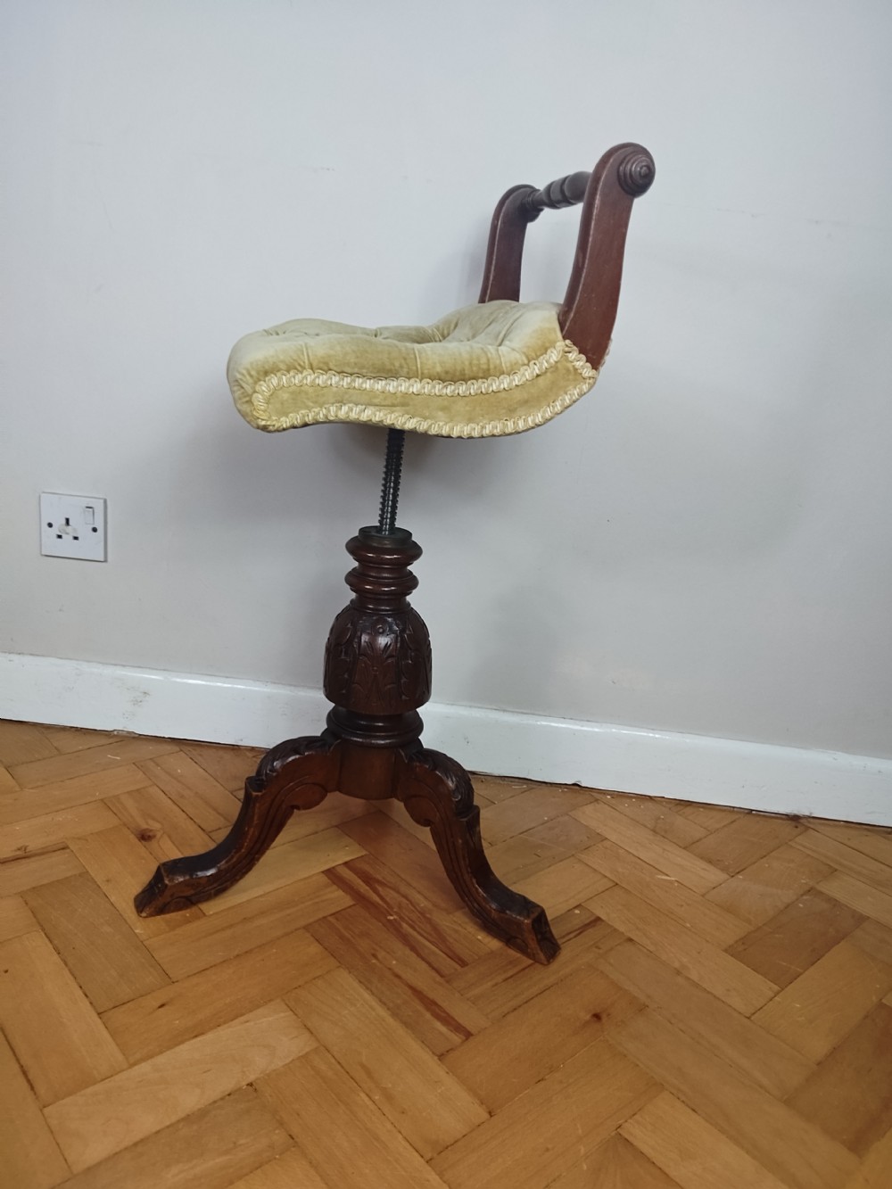 Victorian carved walnut swivel piano stool featuring a button-tufted olive green velvet seat with decorative braid trim and a low curved backrest. View X