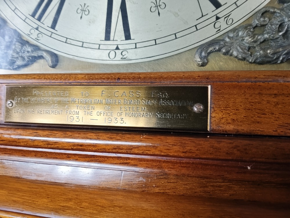 A tall mahogany longcase clock featuring an arched hood, glass door displaying a brass dial with silvered chapter ring, fluted side columns, and a moulded plinth base. View X