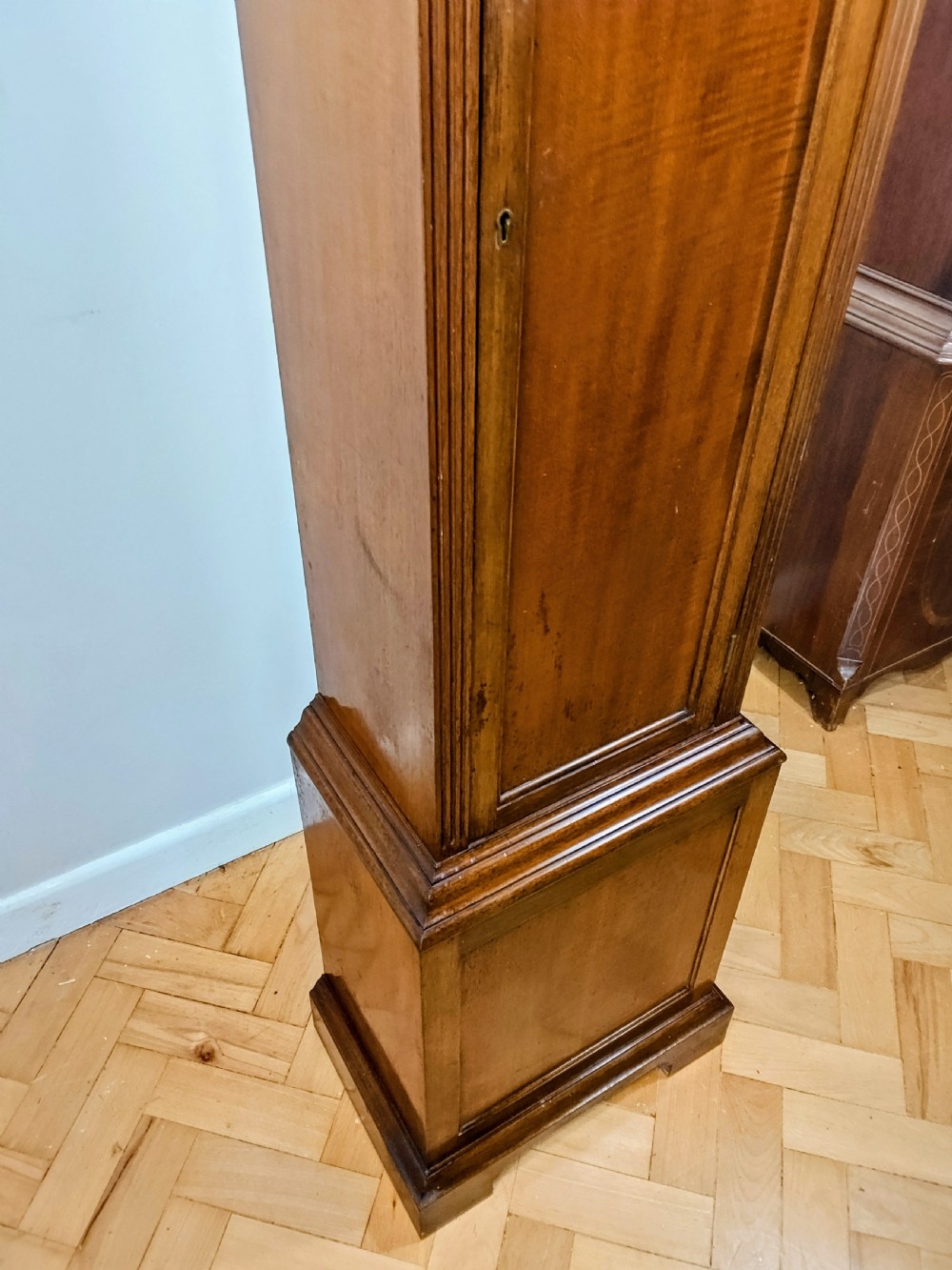 A tall mahogany longcase clock featuring an arched hood, glass door displaying a brass dial with silvered chapter ring, fluted side columns, and a moulded plinth base. View XI