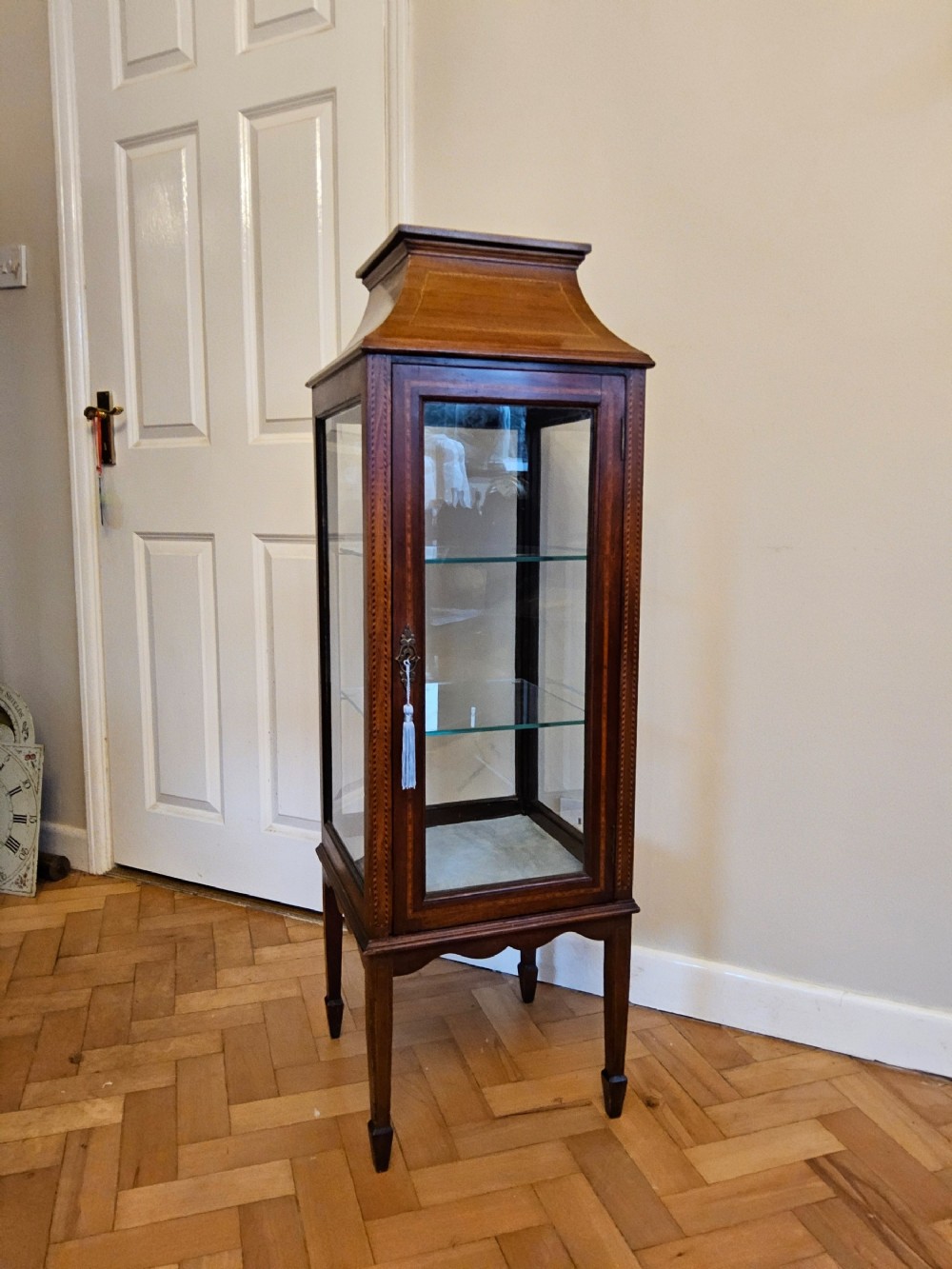 A slender mahogany bijouterie cabinet featuring four glass sides, two glass shelves, satinwood inlay details, and a stepped pagoda top.