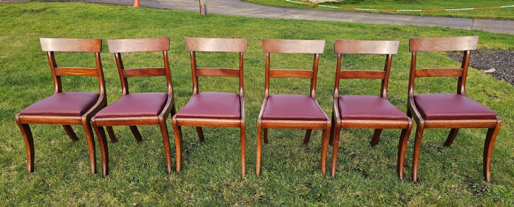 A matching set of six Regency mahogany dining chairs featuring curved sabre legs, horizontal bar backs, and burgundy leather seats.