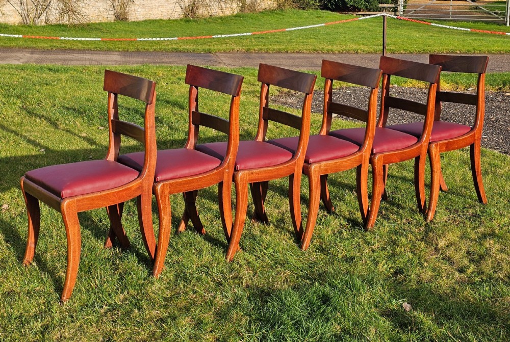 A matching set of six Regency mahogany dining chairs featuring curved sabre legs, horizontal bar backs, and burgundy leather seats. View II