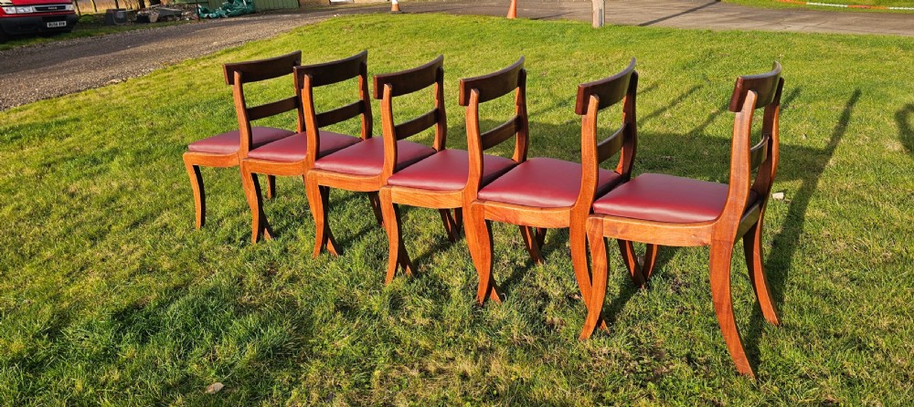 A matching set of six Regency mahogany dining chairs featuring curved sabre legs, horizontal bar backs, and burgundy leather seats. View IV