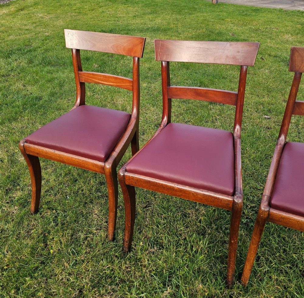 A matching set of six Regency mahogany dining chairs featuring curved sabre legs, horizontal bar backs, and burgundy leather seats. View VI