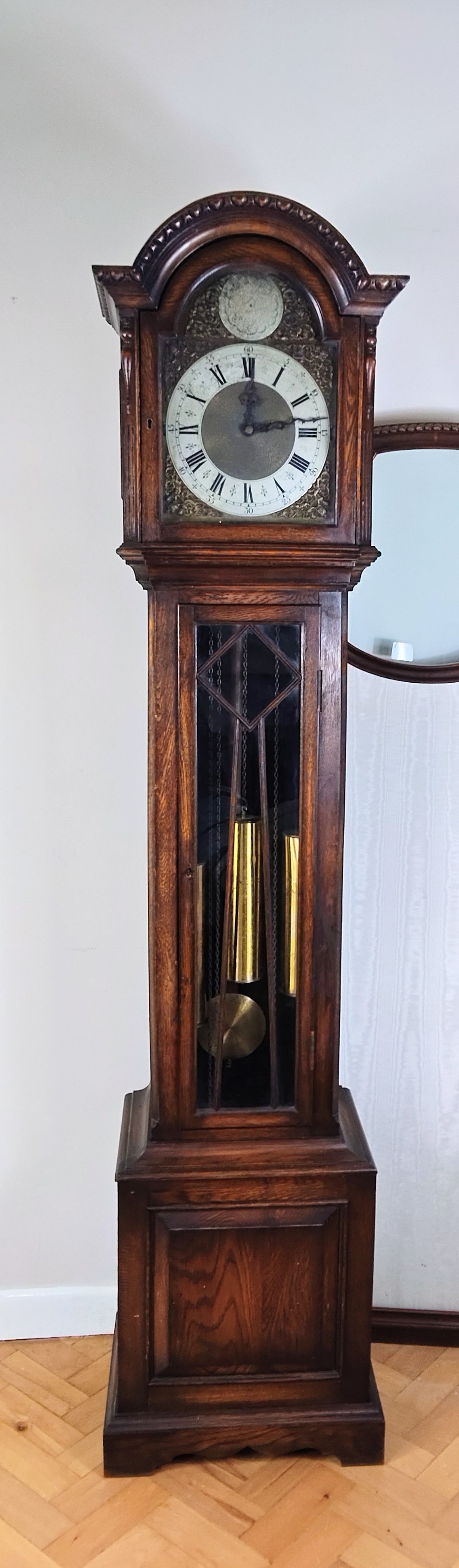 A dark oak longcase clock featuring an arched hood, a brass dial with silvered chapter ring, and an astragal glazed trunk door.