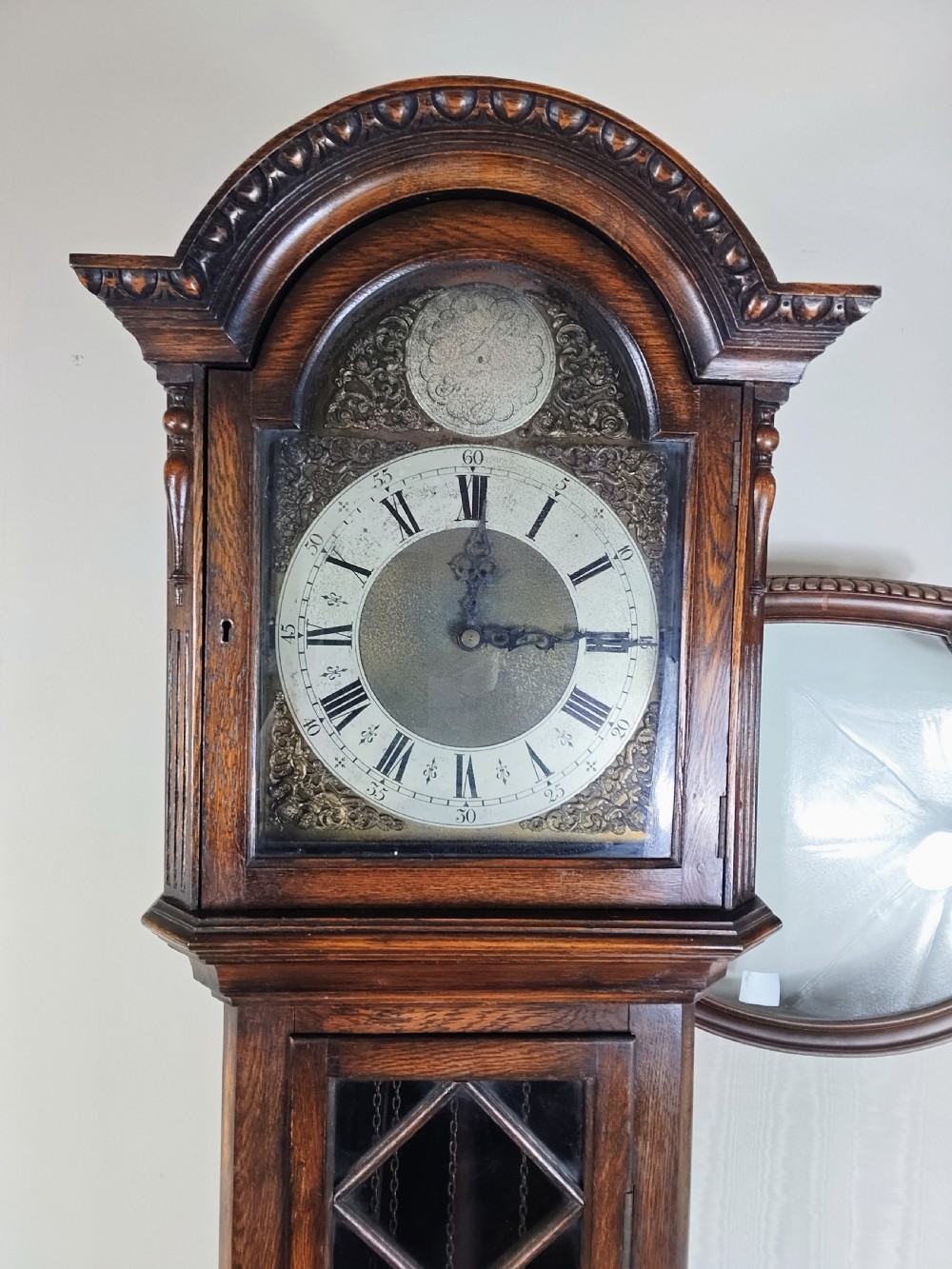 A dark oak longcase clock featuring an arched hood, a brass dial with silvered chapter ring, and an astragal glazed trunk door. View IV