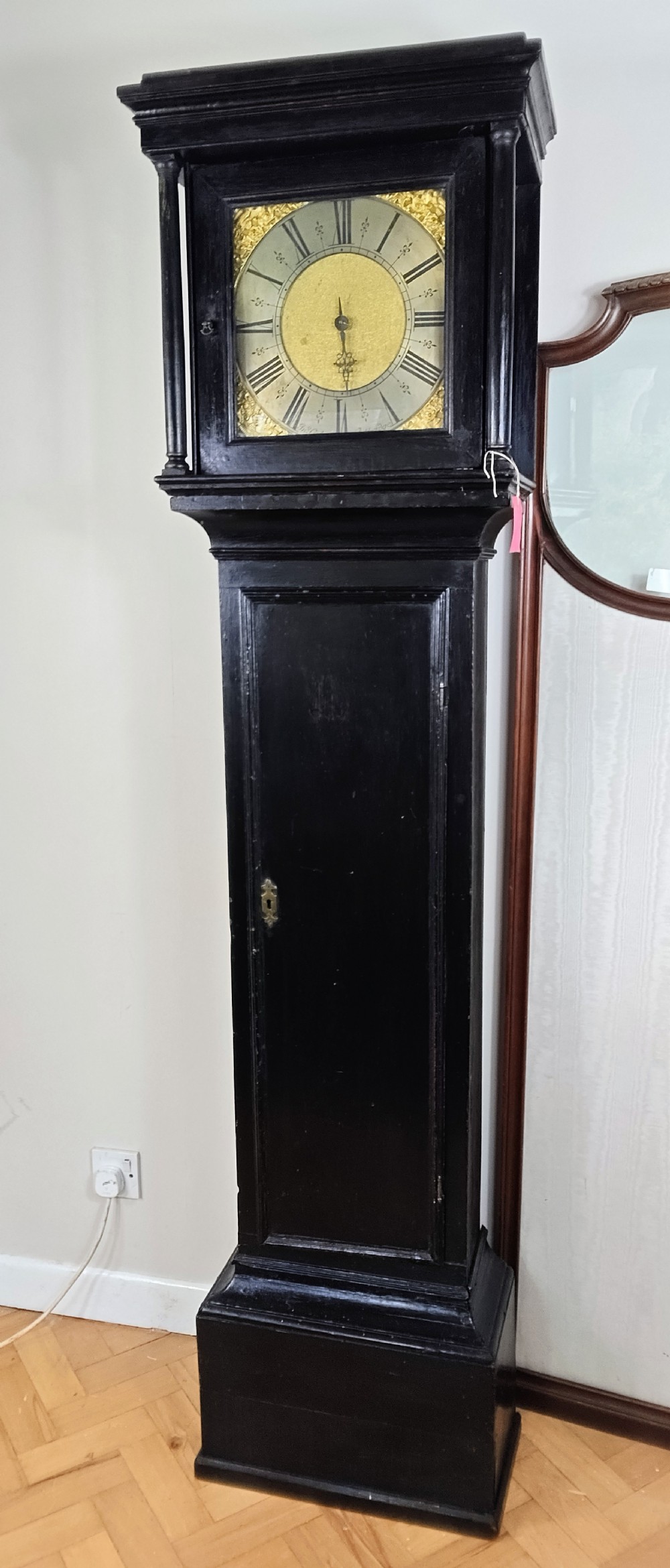 An antique Queen Anne ebonised longcase clock featuring a square brass dial with Roman numerals and ornate corner spandrels.
