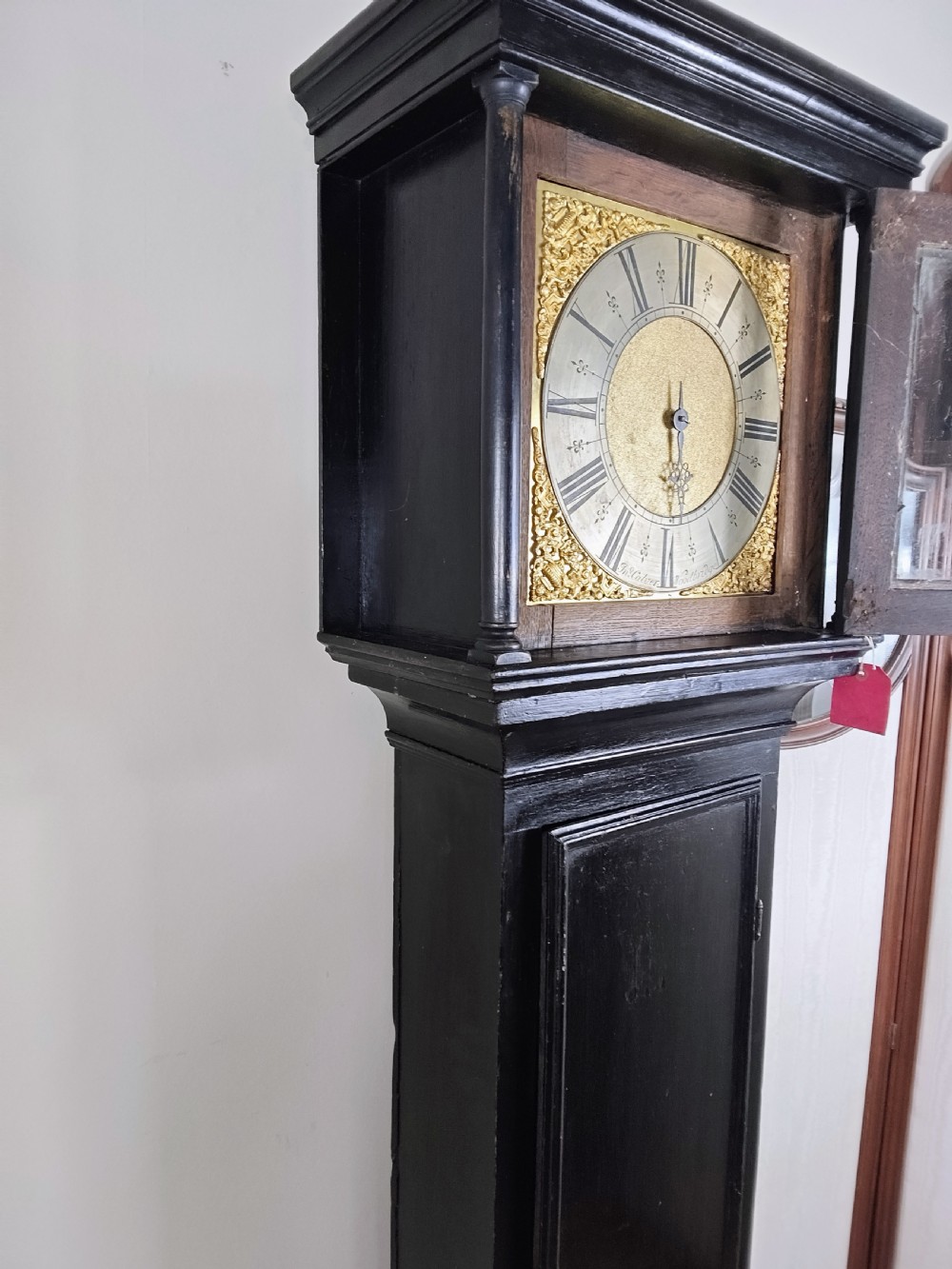 An antique Queen Anne ebonised longcase clock featuring a square brass dial with Roman numerals and ornate corner spandrels. View XIV