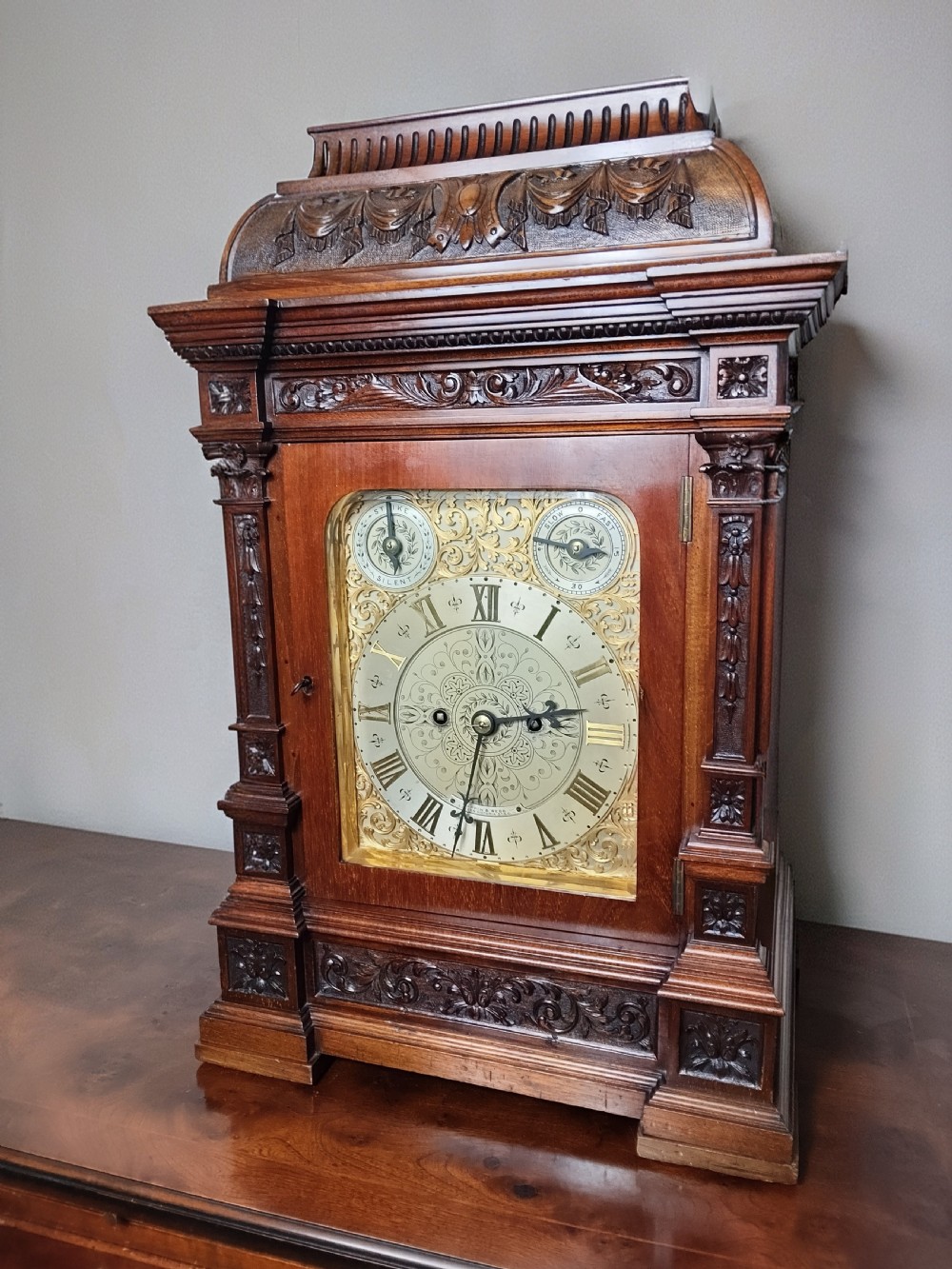 A Victorian carved mahogany twin fusee table clock featuring an ornate brass dial with silvered chapter ring and carved column details.