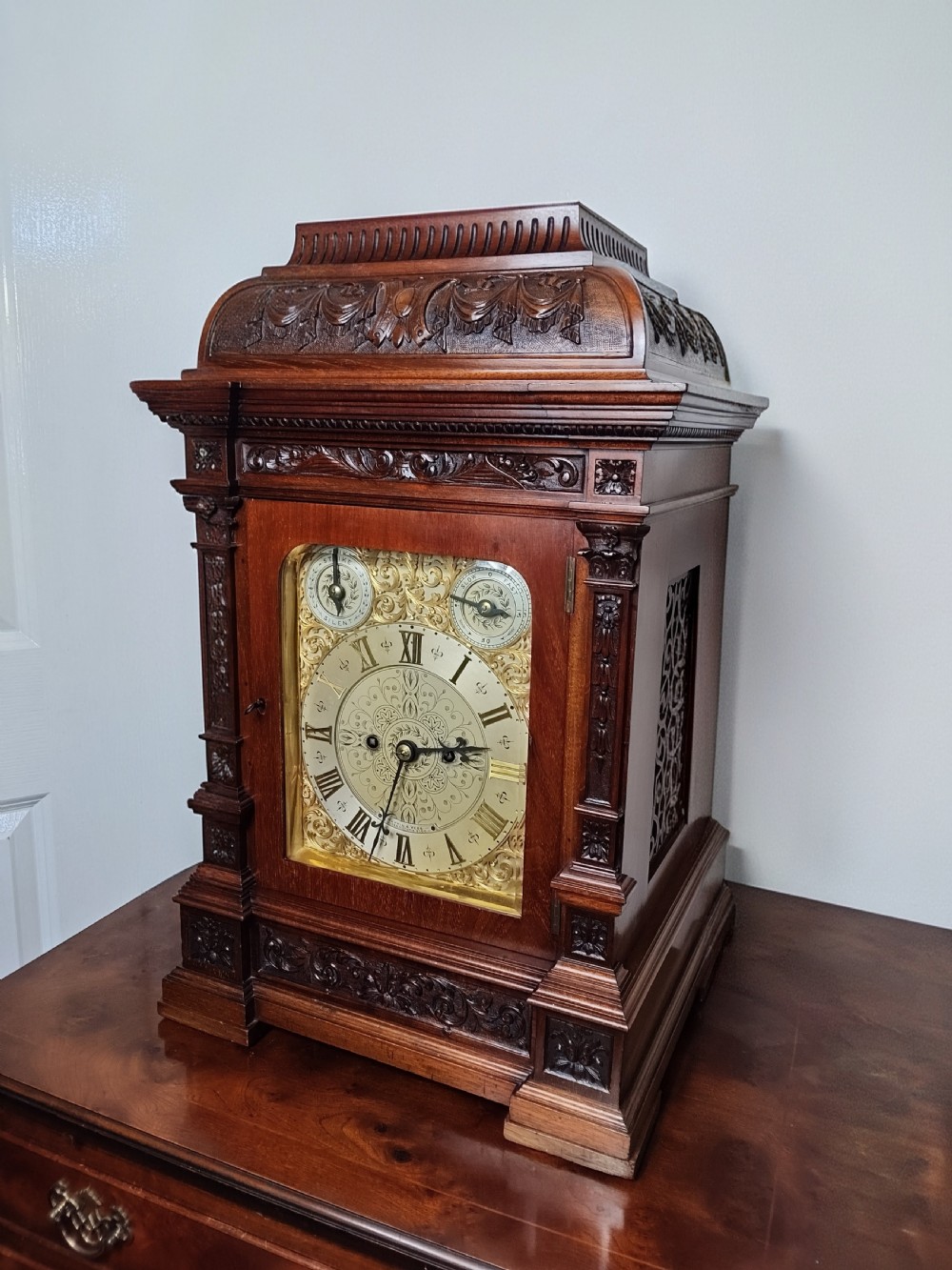 A Victorian carved mahogany twin fusee table clock featuring an ornate brass dial with silvered chapter ring and carved column details. View XIV