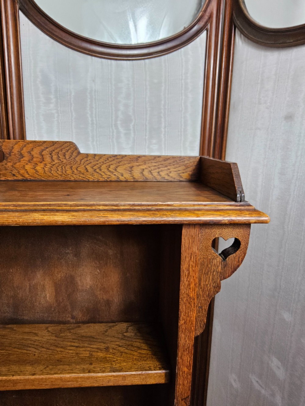 An Arts and Crafts solid oak open bookcase featuring three shelves and heart-shaped cutouts on the top gallery and side brackets. View IV