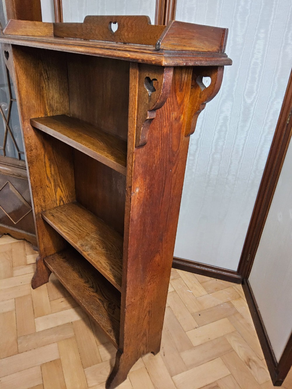An Arts and Crafts solid oak open bookcase featuring three shelves and heart-shaped cutouts on the top gallery and side brackets. View V