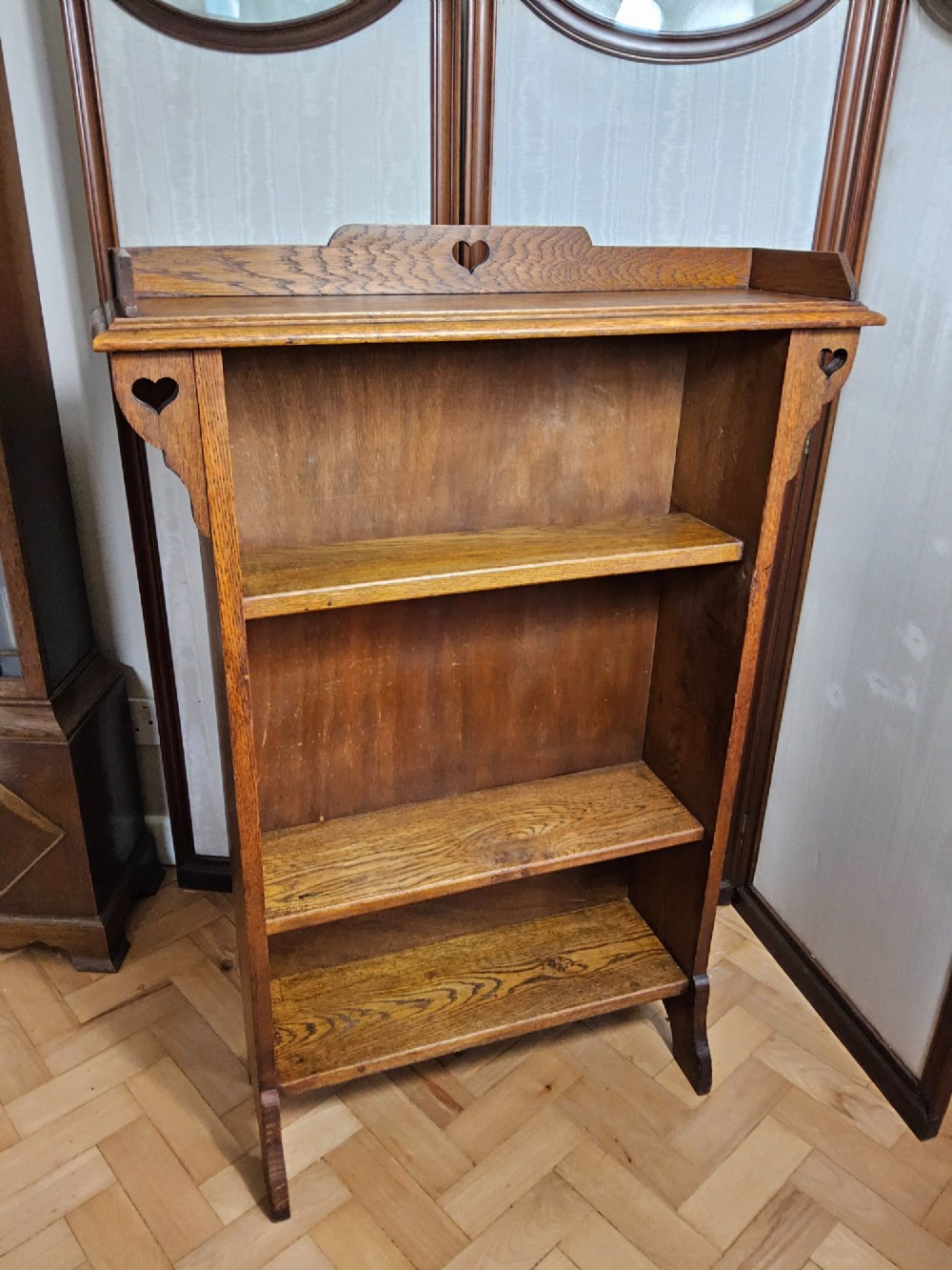 An Arts and Crafts solid oak open bookcase featuring three shelves and heart-shaped cutouts on the top gallery and side brackets. View VIII