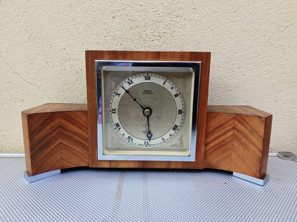 An Art Deco walnut mantel clock featuring chevron-patterned wooden wings, a central square face with Roman numerals, and chrome trim accents.