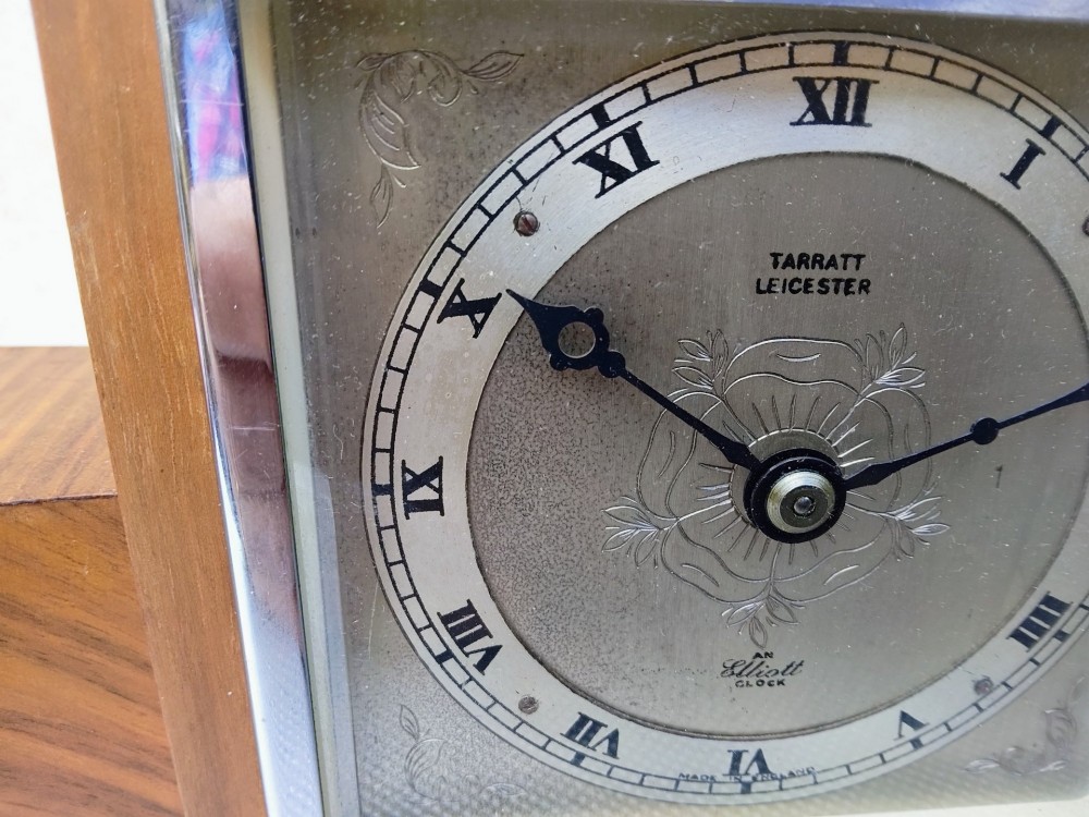 An Art Deco walnut mantel clock featuring chevron-patterned wooden wings, a central square face with Roman numerals, and chrome trim accents. View III